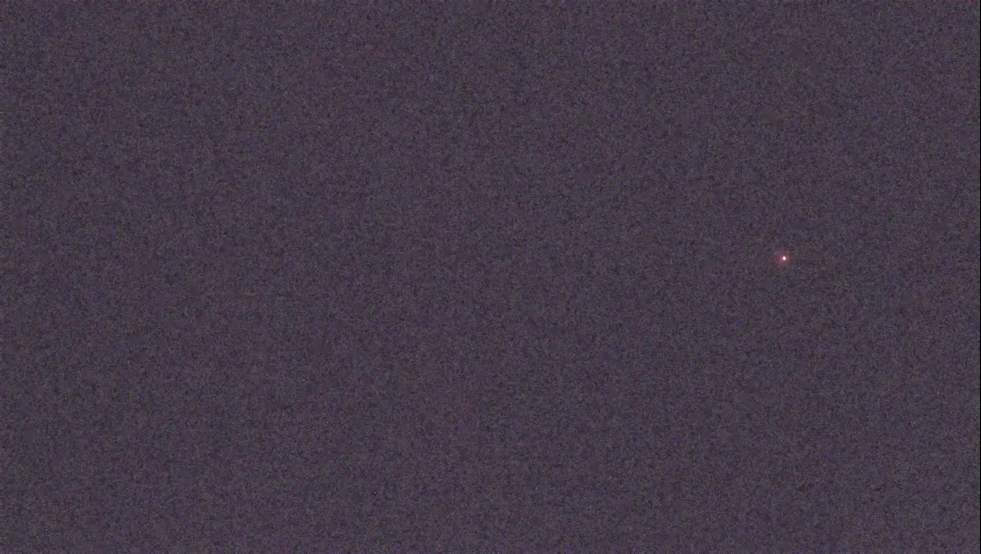 A single, small, reddish light is visible in a dark, textured sky.