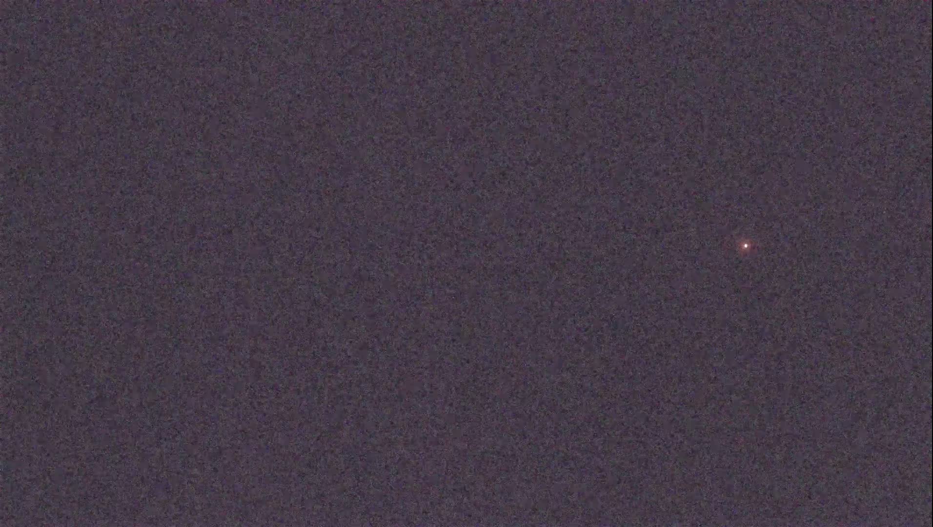 A single, small, reddish light is visible in a dark, night sky.