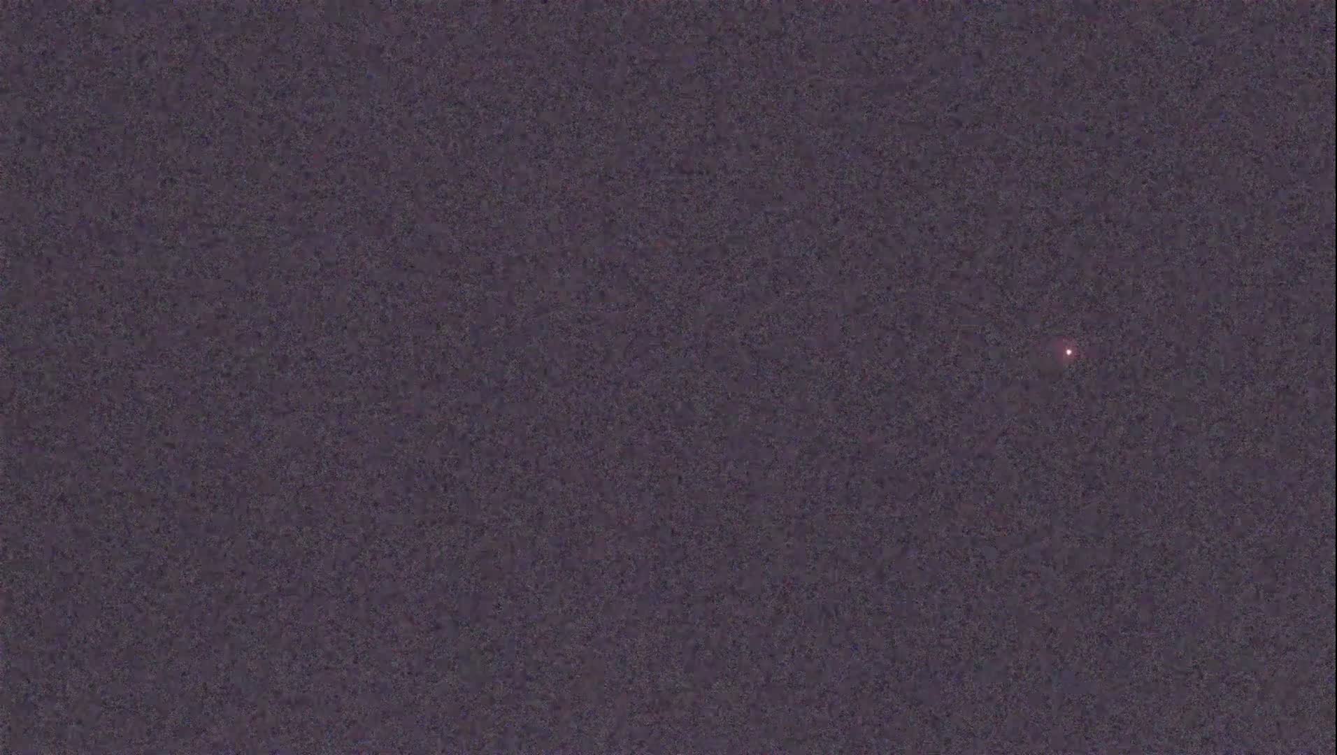 A single, small, reddish light is visible against a dark, mottled, nighttime sky.
