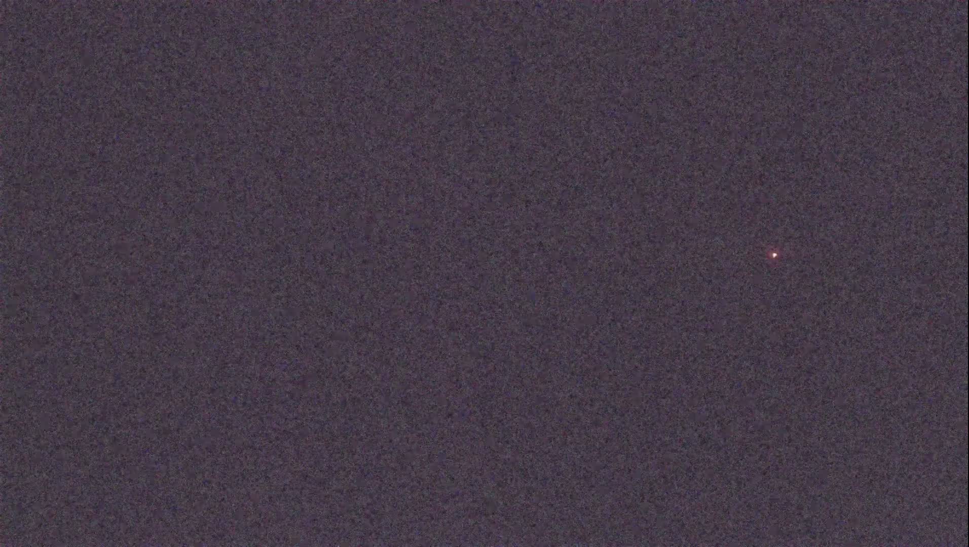 A small, faint, reddish light is visible in a dark, grainy sky.