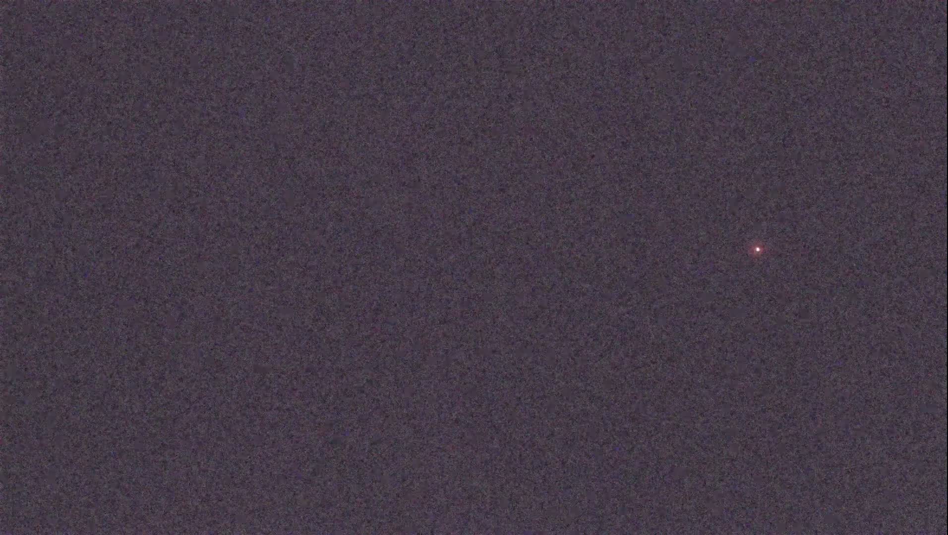 A single, small, reddish light is visible in a dark, night sky.