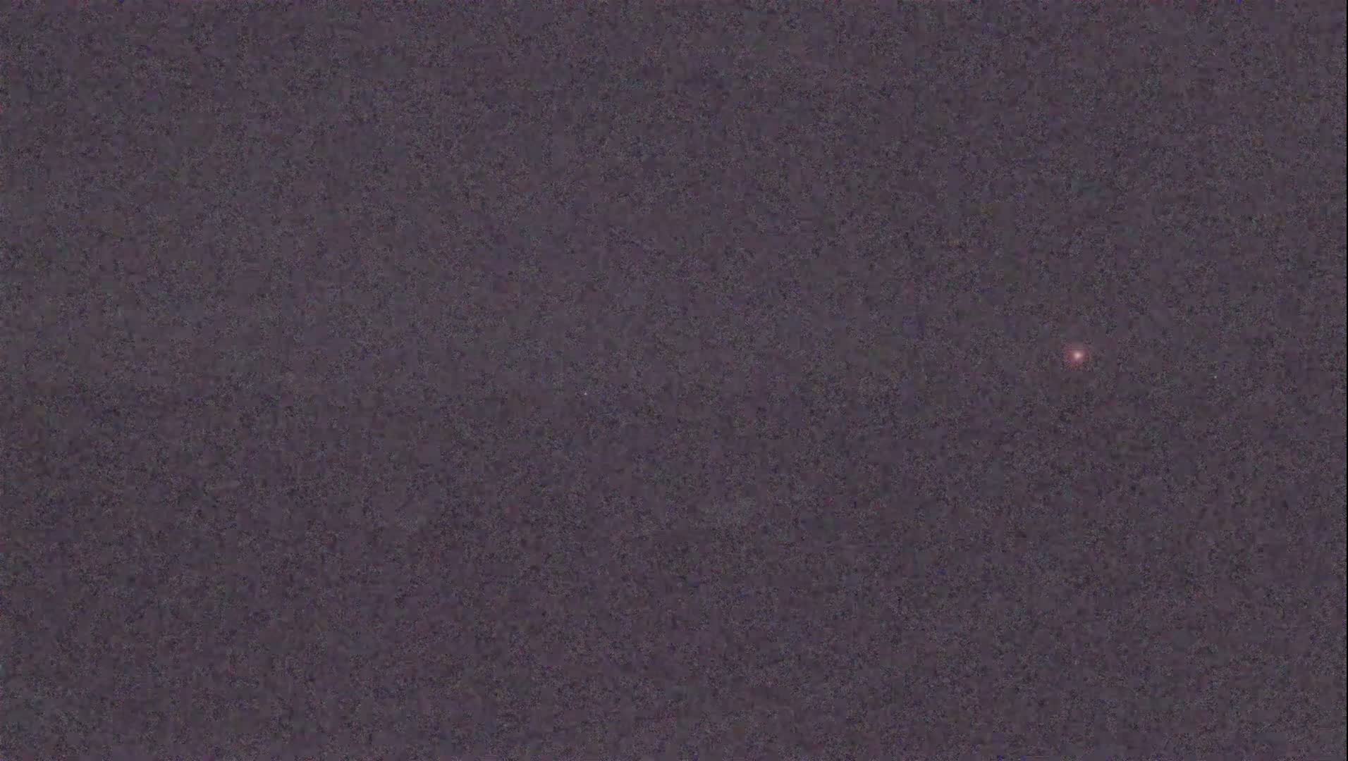 A single, small, reddish light is visible against a dark, grainy, night sky.