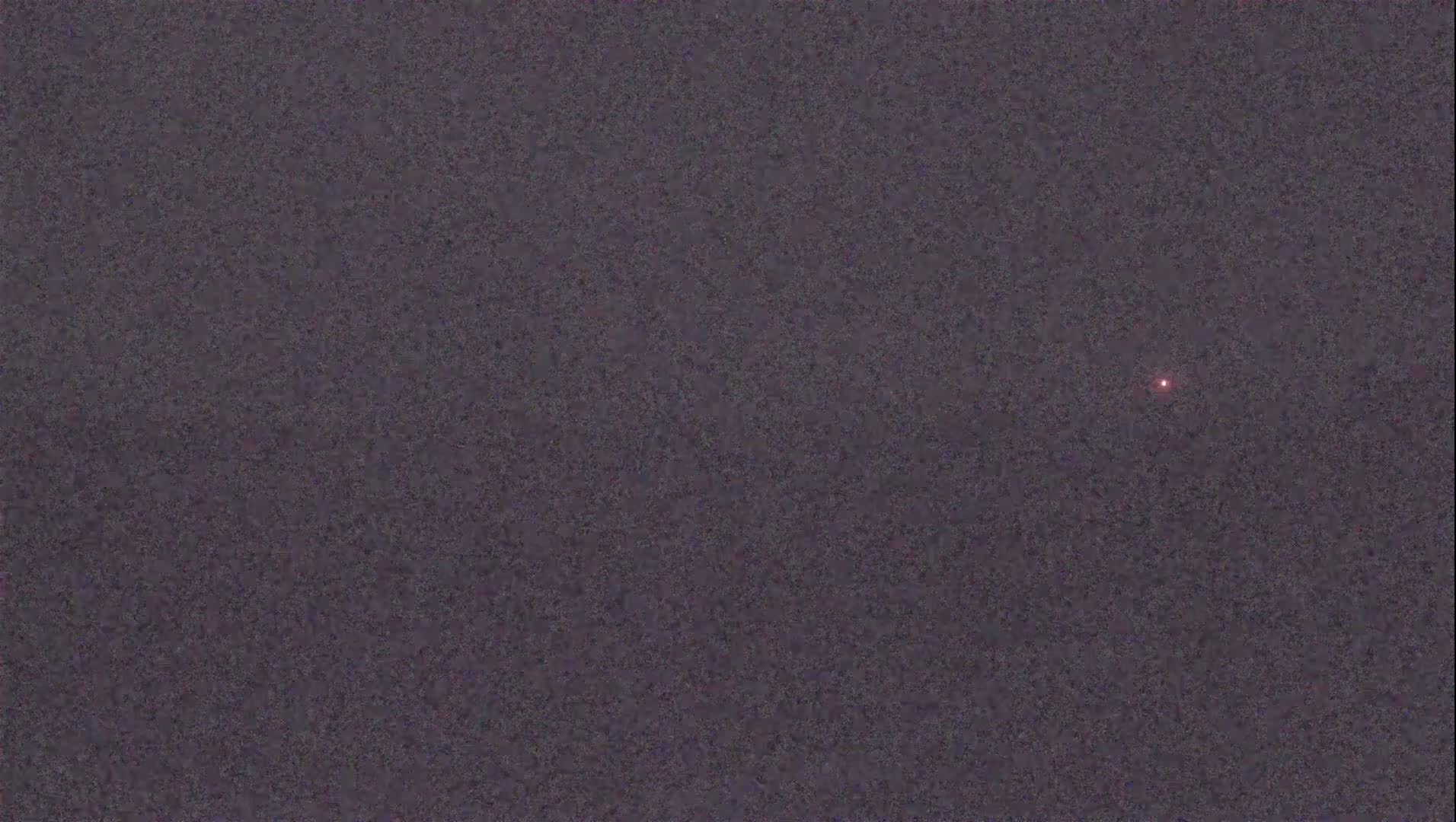 A single, small, reddish light is visible in a dark, textured sky.