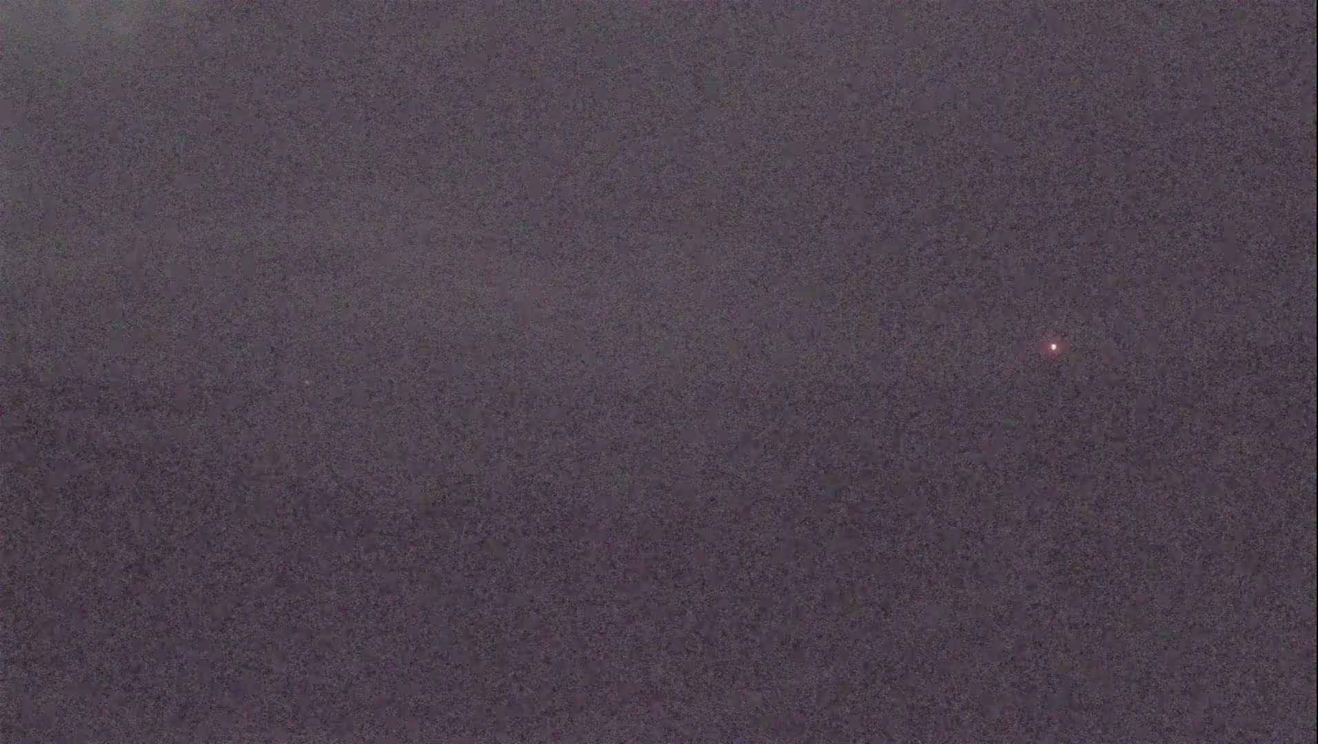 A small, dim red light is visible against a dark, textured gray sky.