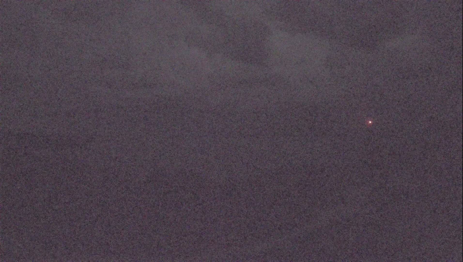 A small, dim, reddish light is visible in a dark, overcast sky.