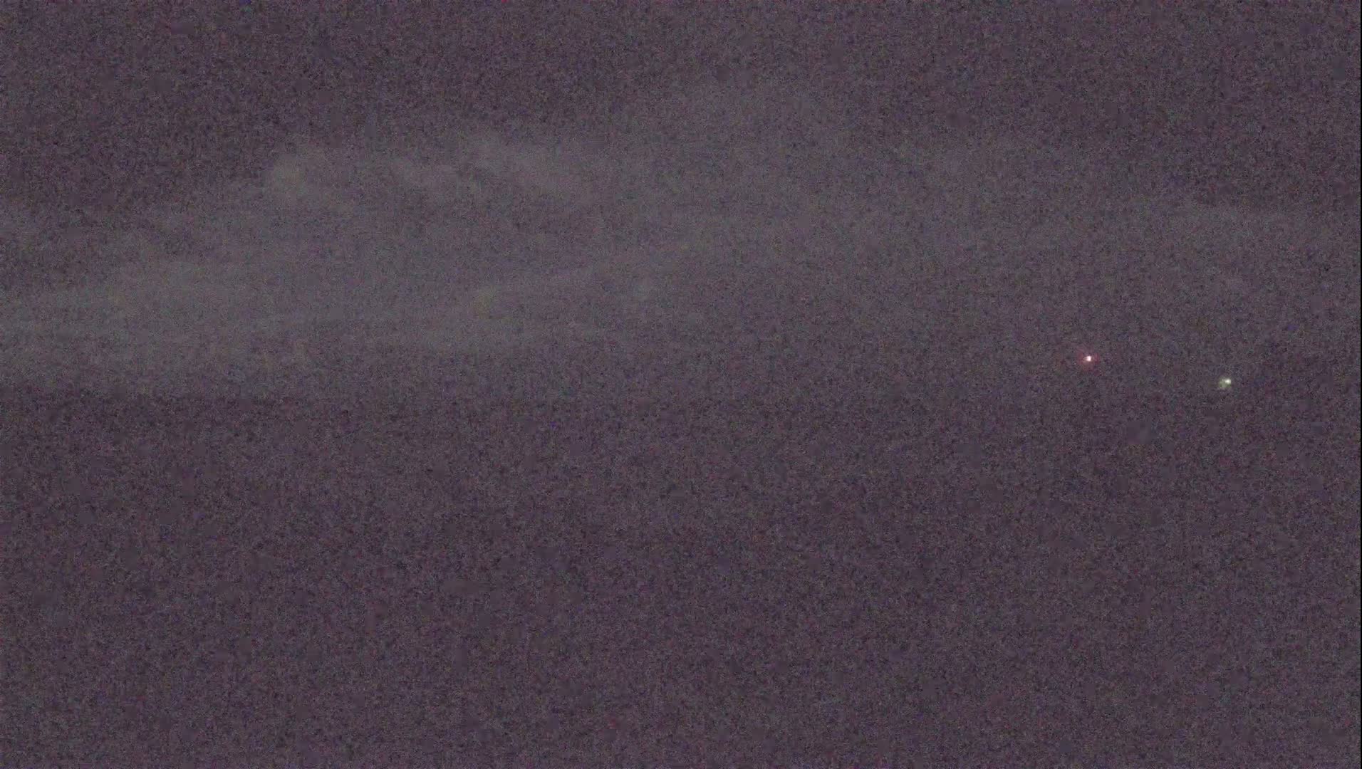 A dark, cloudy night sky shows a faint, distant mountain range and two small lights.