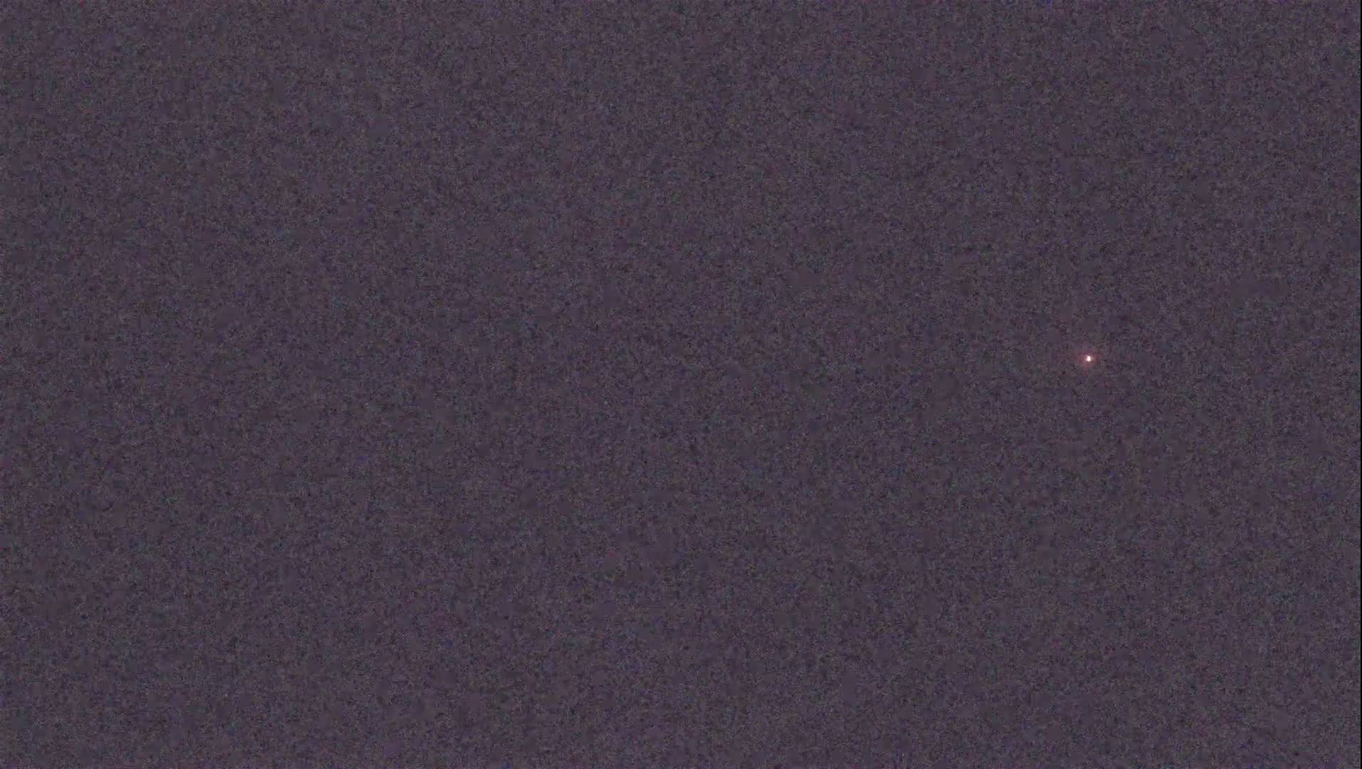A small, reddish light is visible in a dark, grainy sky.