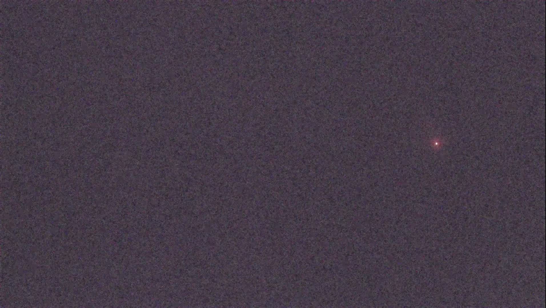 A single, small, red light is visible in a dark, night sky.