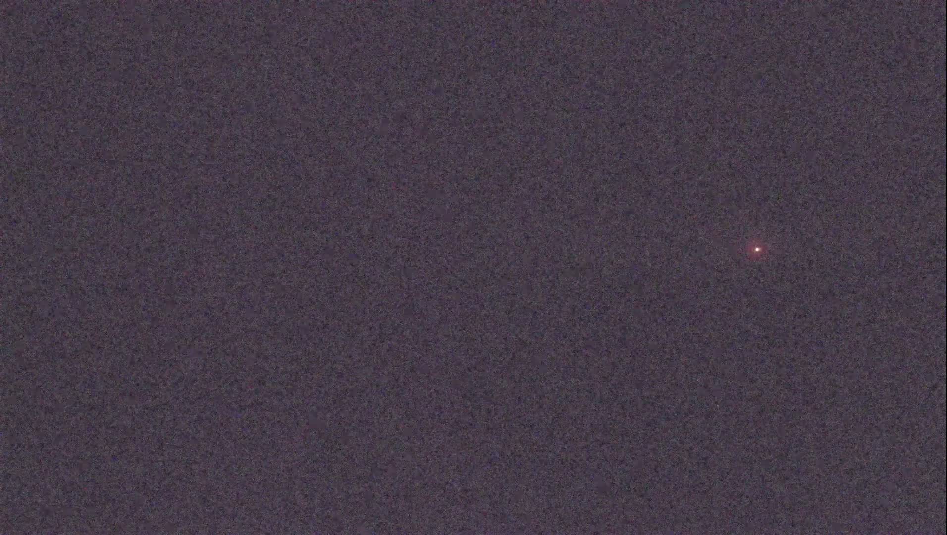 A single, small, reddish light is visible in a dark, night sky.