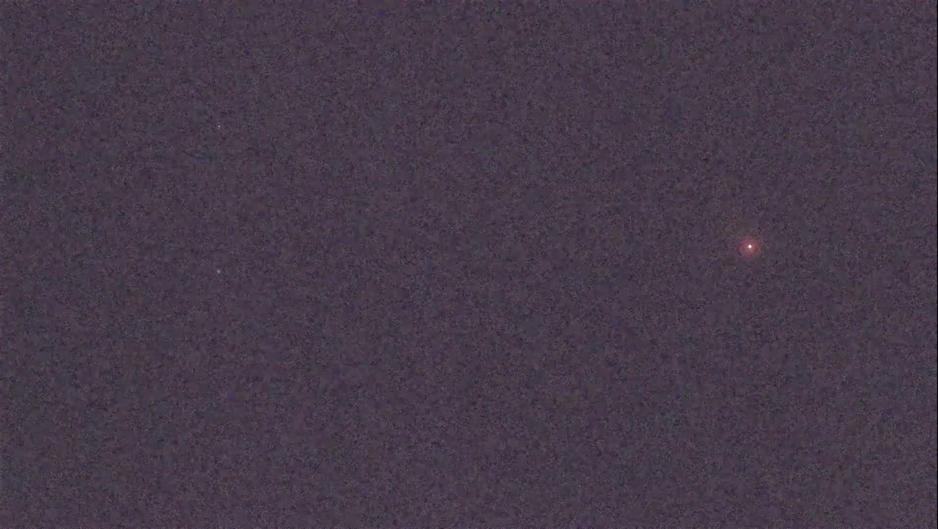 A single, small, reddish light is visible in a dark, night sky.