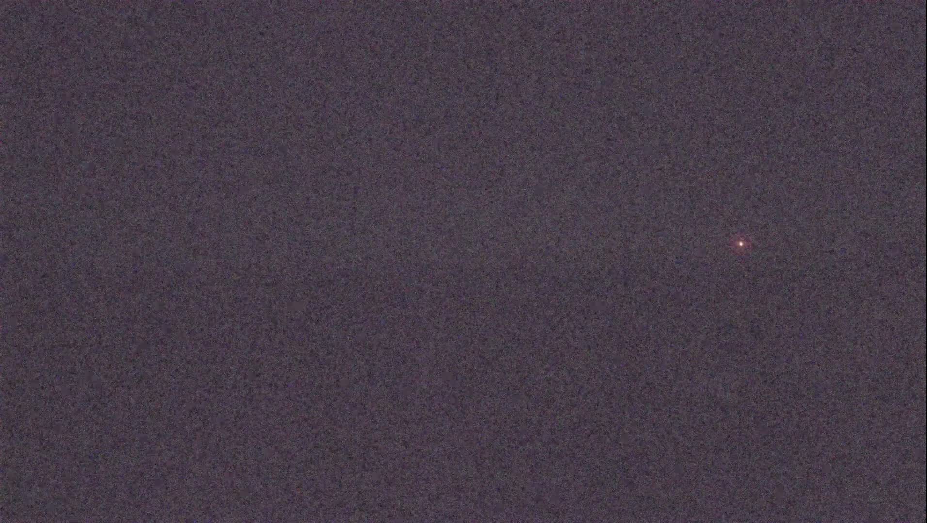 A single, small, reddish light is visible in a dark, grainy sky.