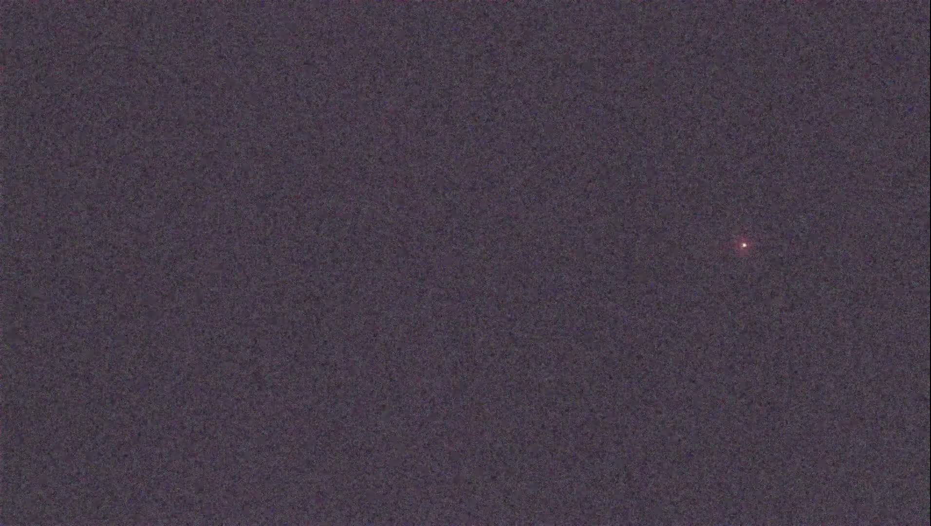 A single, small, reddish light is visible in a dark, night sky.