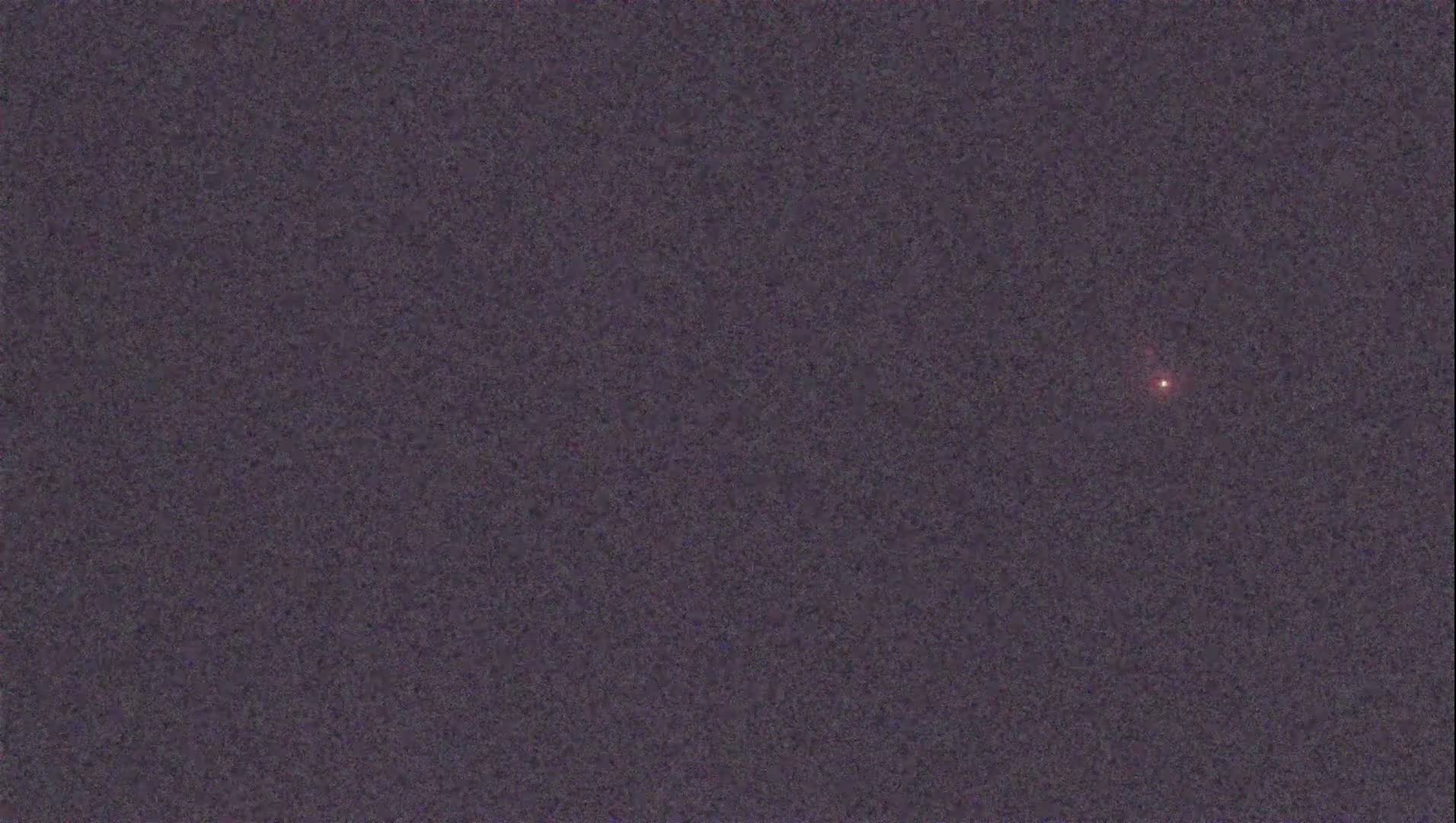 A single, faint, reddish light is visible in a dark, night sky.