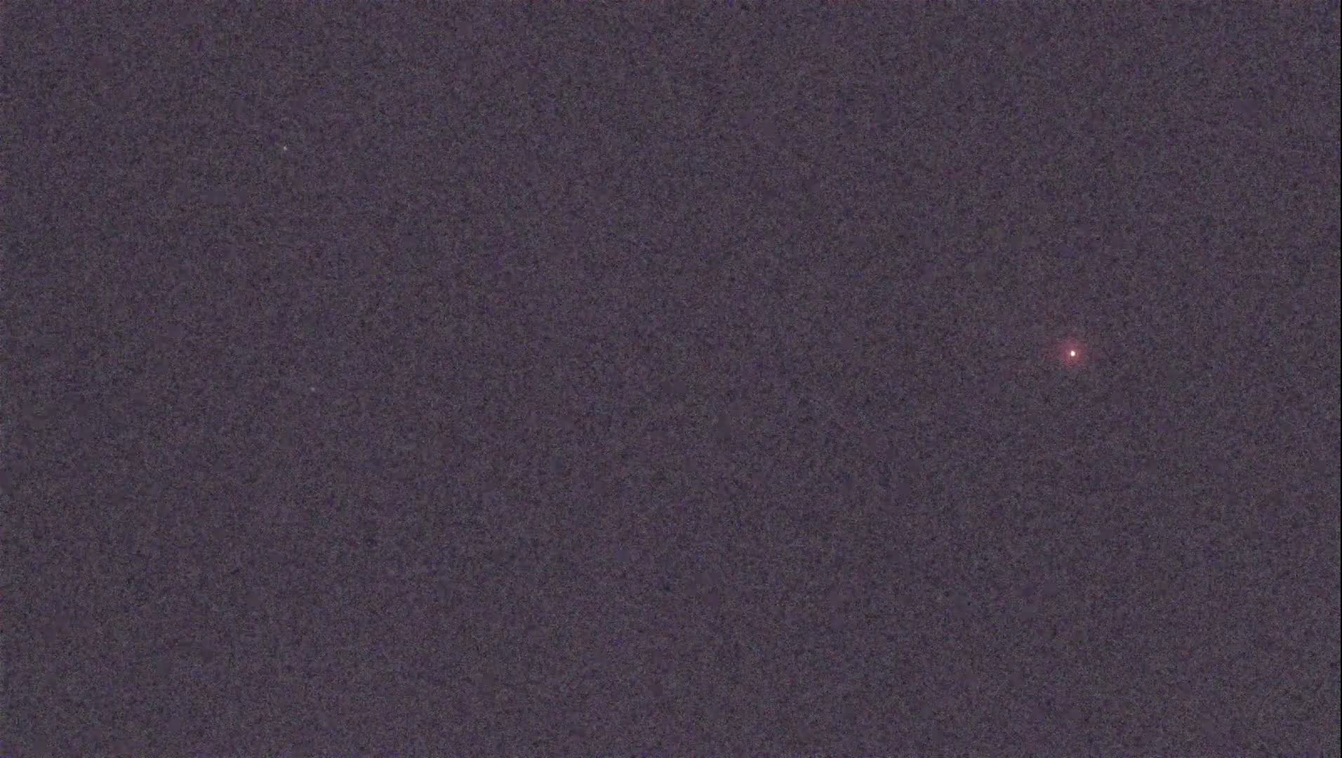 A single, faint, reddish light is visible in a dark, night sky.