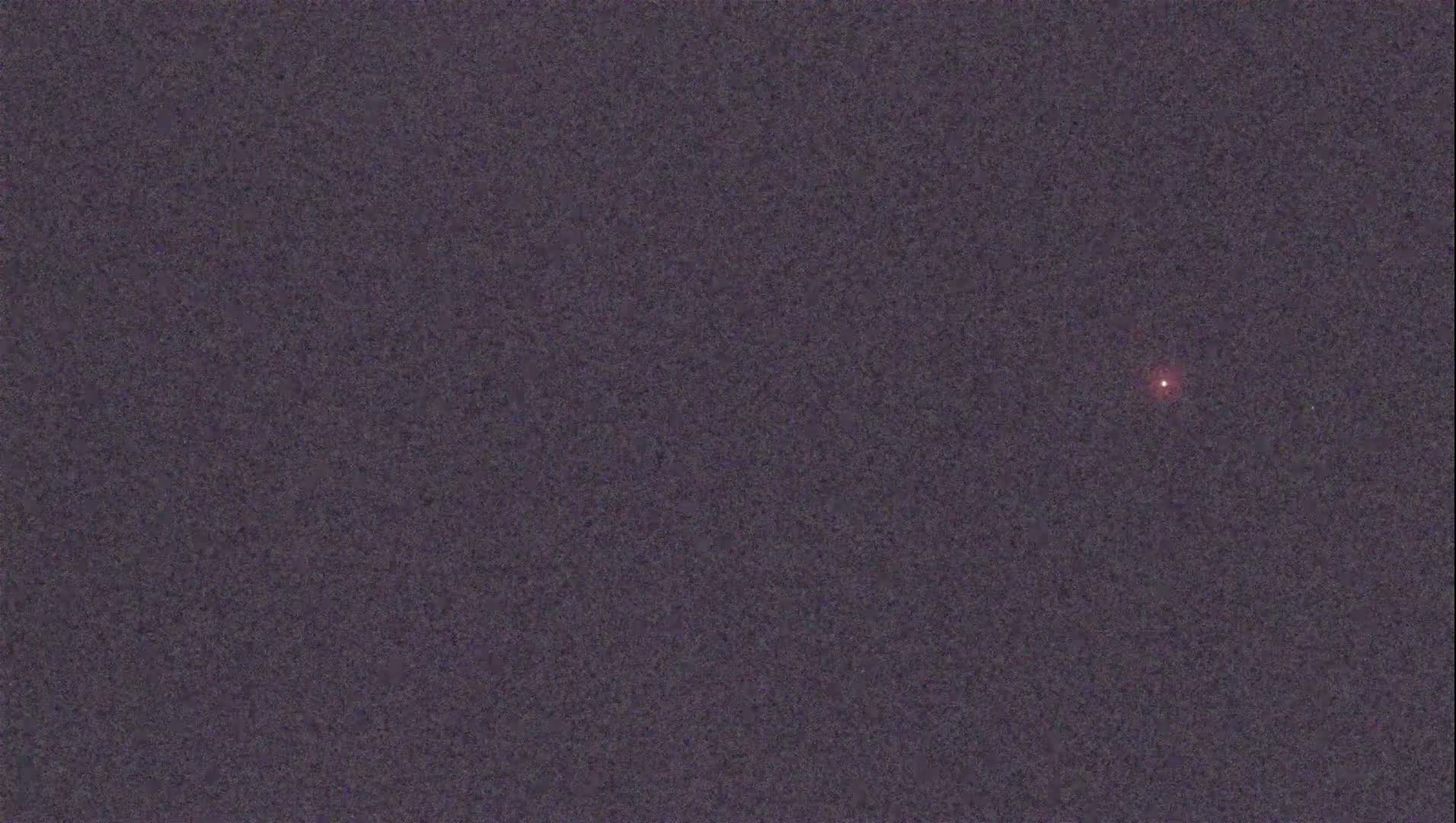 A single, faint reddish light is visible in a dark, night sky.