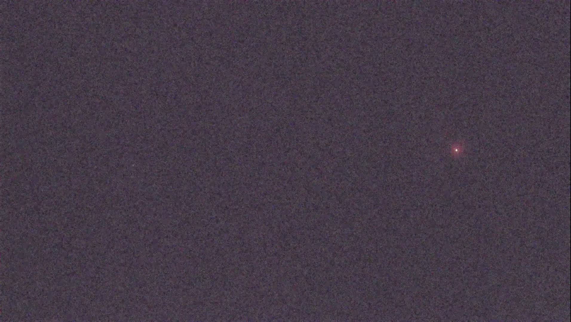 A single, small, reddish light is visible against a dark, textured purple background.
