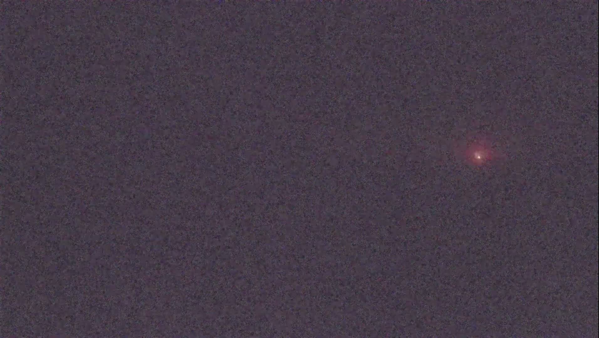 A small, reddish light is visible in a dark, night sky.