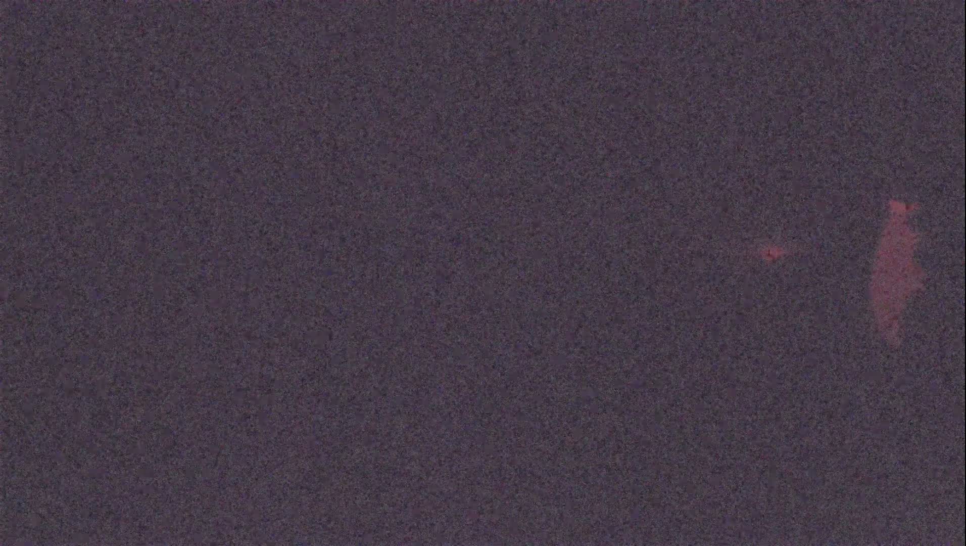A dark gray textured surface with faint, blurry reddish blotches.