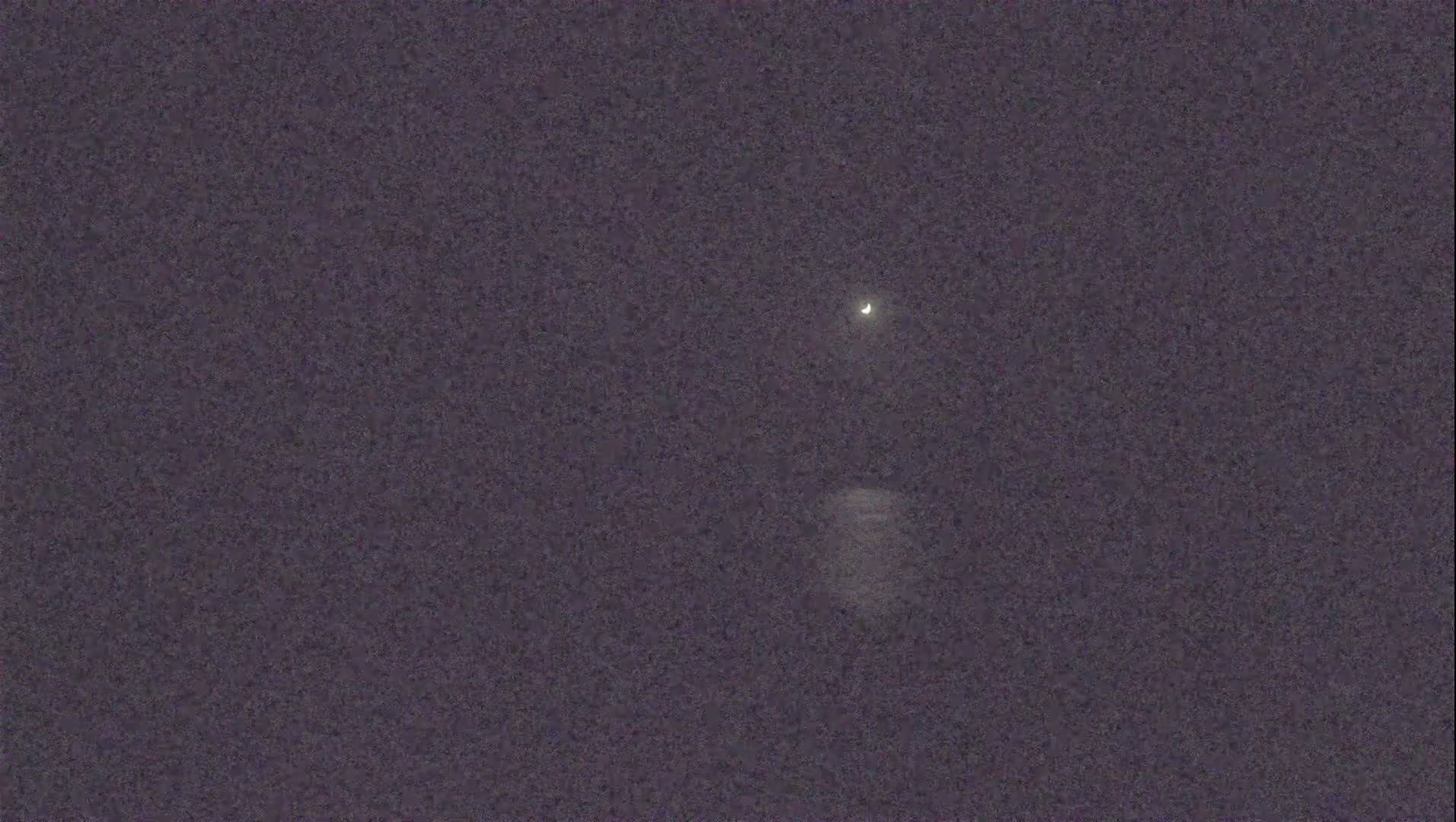 A crescent moon and a brighter star are visible in a dark, night sky.