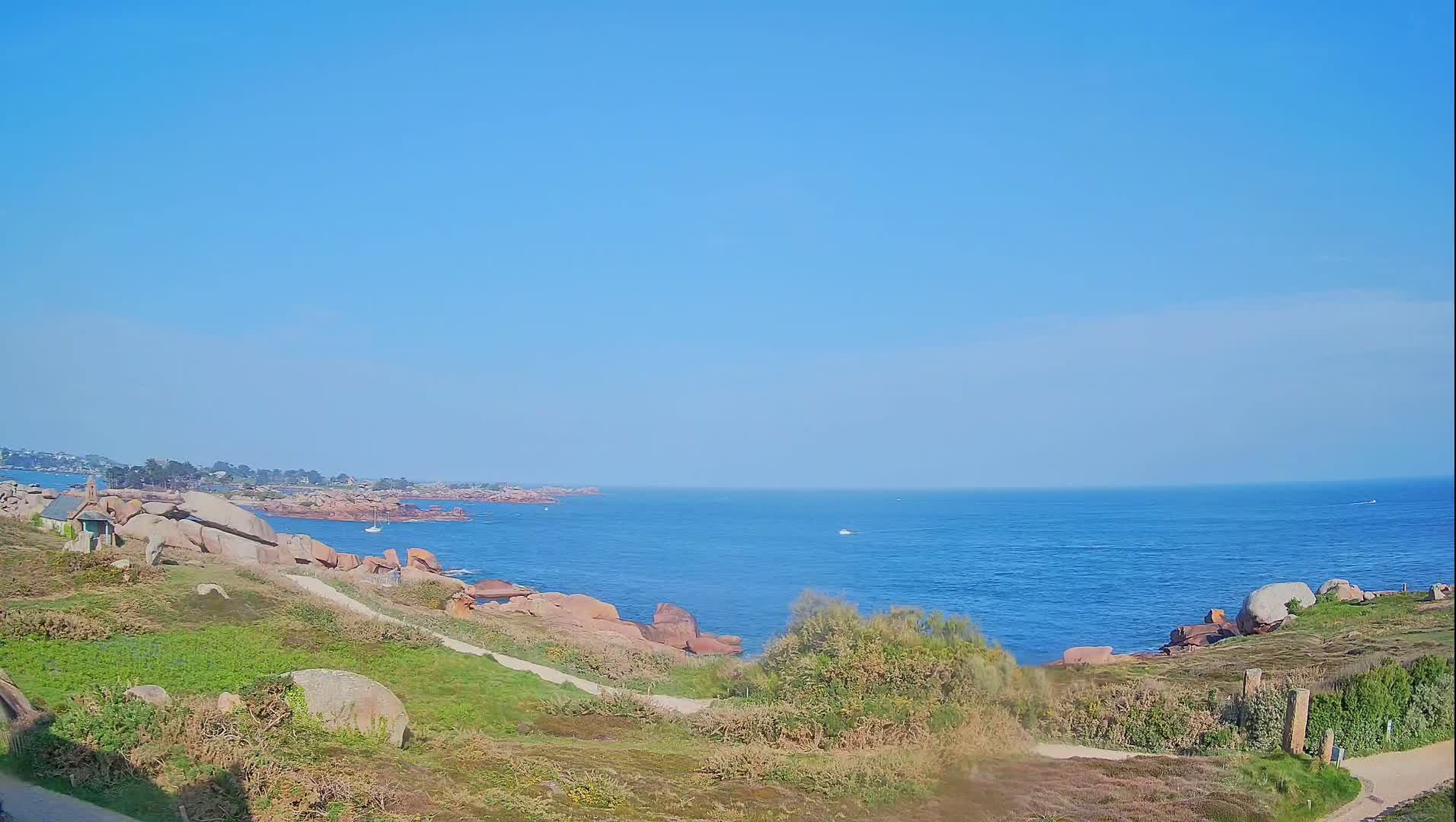 A rocky coastline with grassy hills and a calm blue ocean under a clear sky stretches to a distant horizon.