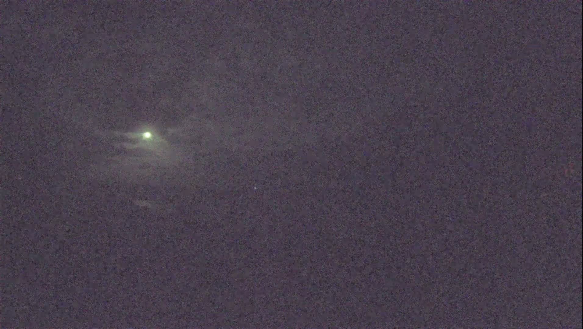 A partially clouded night sky shows a bright moon and a few faint stars.