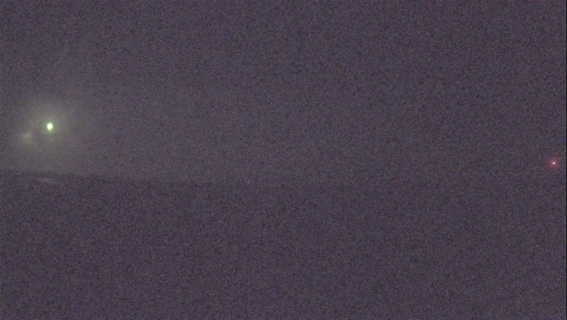 A nighttime, hazy landscape shows a bright light in the upper left and a faint red light in the upper right.