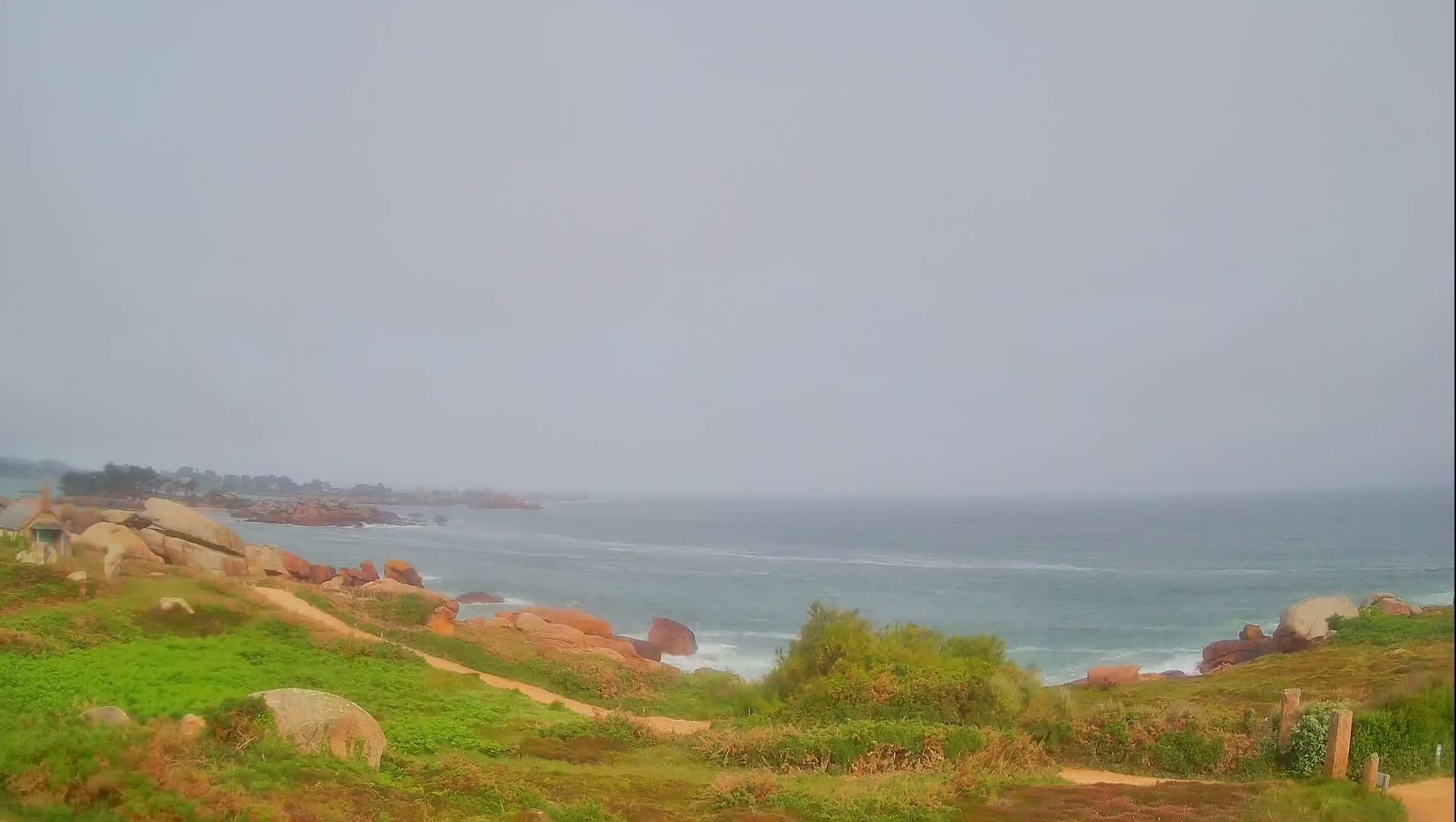 A hazy, overcast day reveals a rocky coastline with a green, grassy hillside sloping down to a choppy sea.