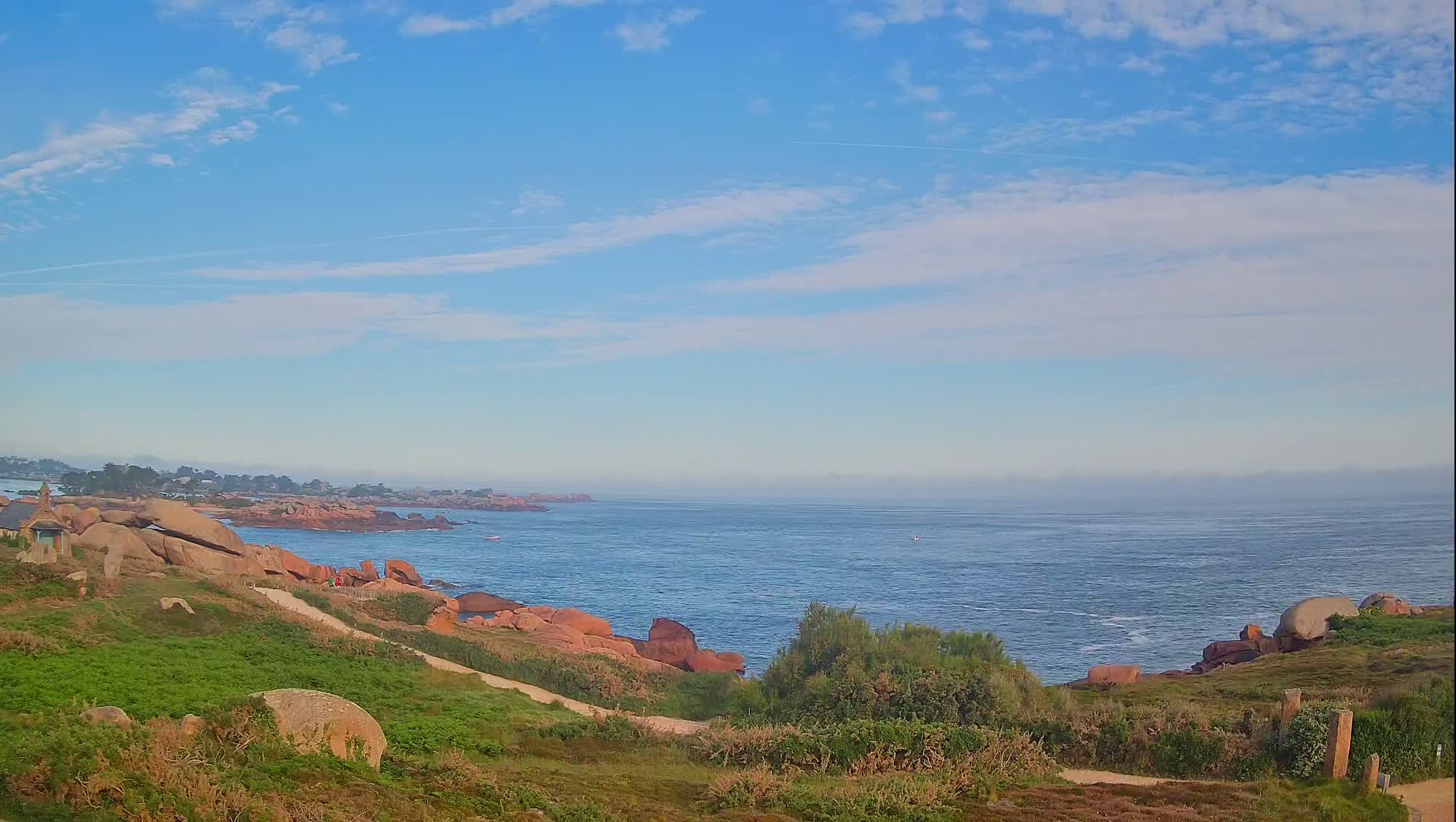 A partly cloudy sky overlooks a rocky coastline and calm ocean.