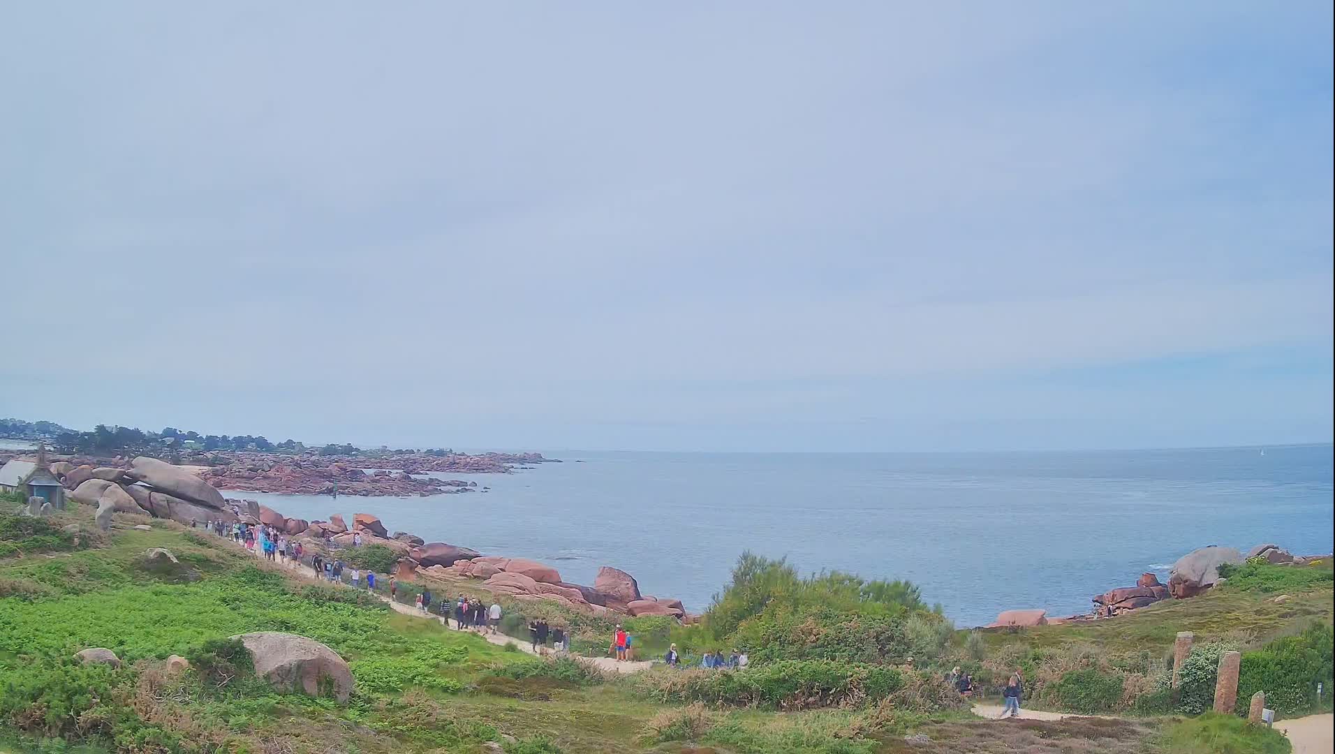 A coastal path winds along a rocky shoreline, where a group of people are walking under a cloudy sky.