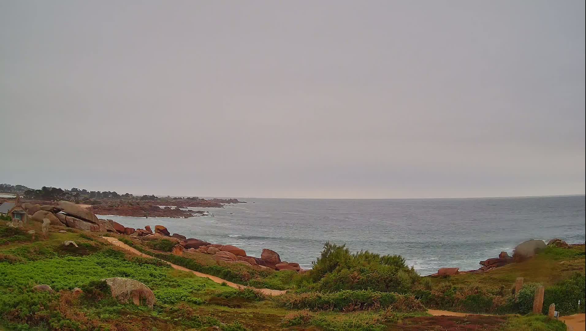 A rocky coastline with a path leading down to the ocean under an overcast sky.