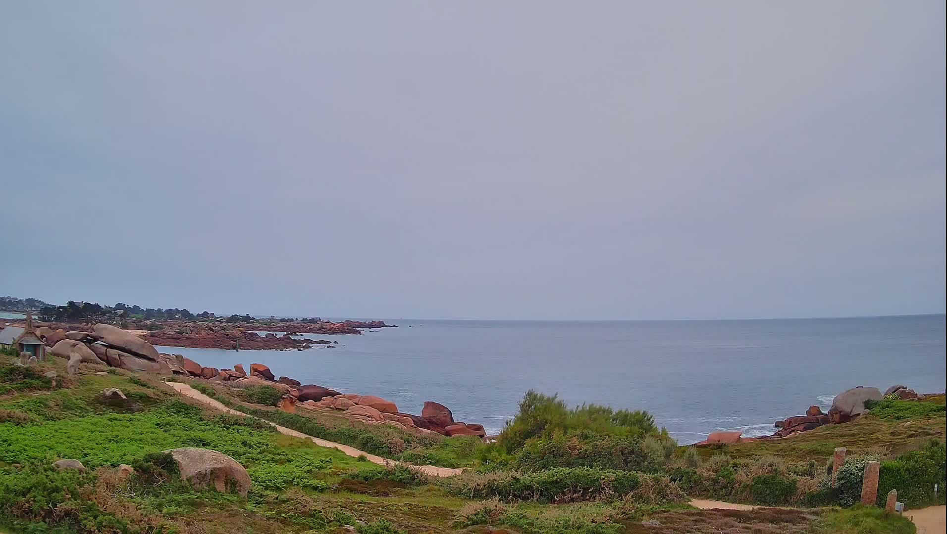 A calm, overcast day reveals a coastal scene with pink and red rocks along a gently sloping shoreline meeting a tranquil ocean.