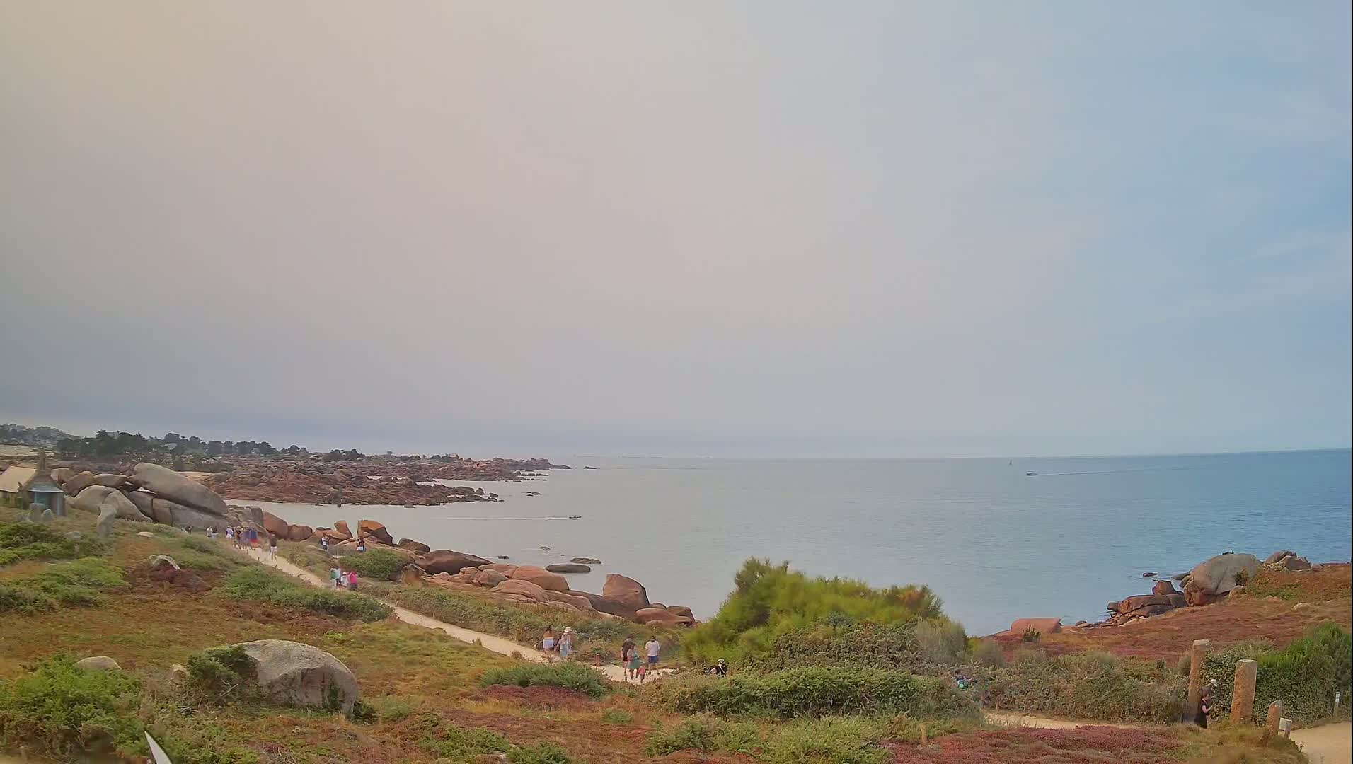 A hazy, overcast coastal scene shows a rocky shoreline with a path leading down to the sea.
