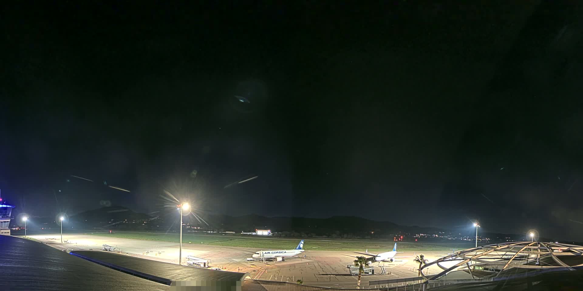 A nighttime view of an airport tarmac with a plane and several ground support vehicles under a clear, dark sky.