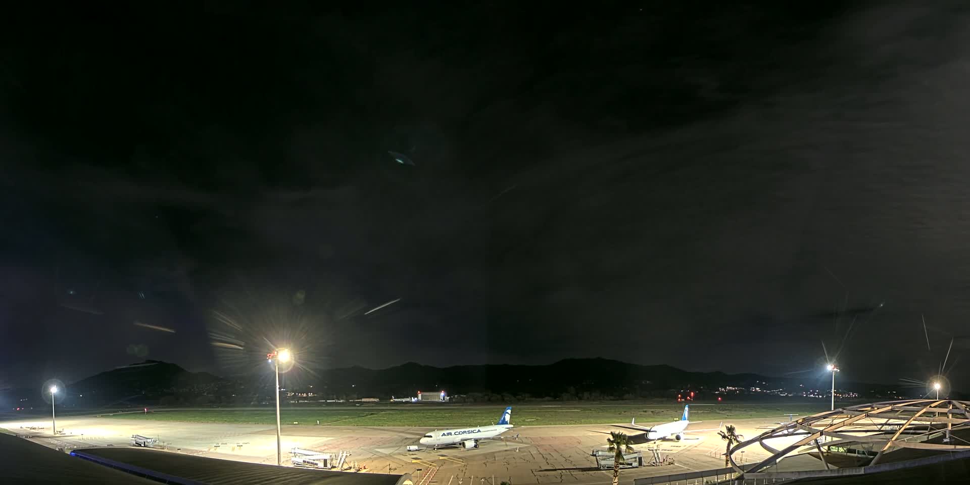 A nighttime view of a mostly empty airport tarmac with two airplanes parked, under a dark, cloudy sky.