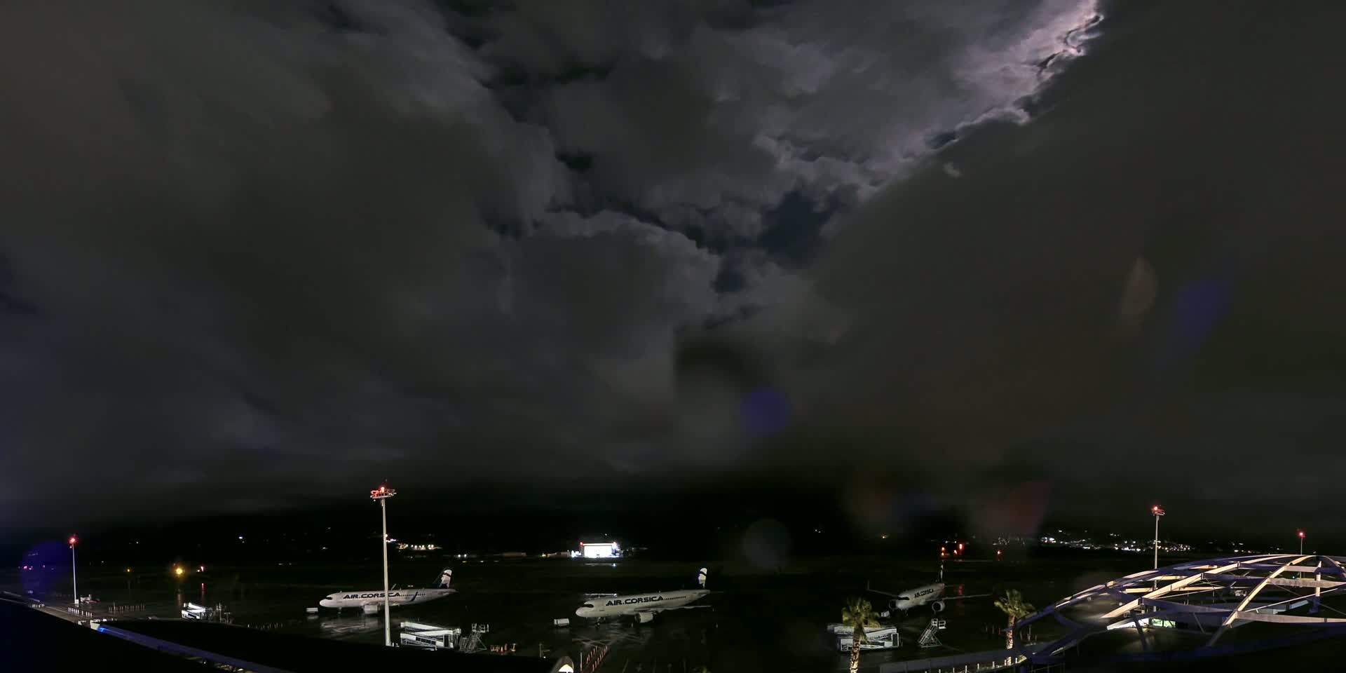 Several airplanes are parked on a dark airport tarmac under a stormy night sky filled with heavy, dark clouds.