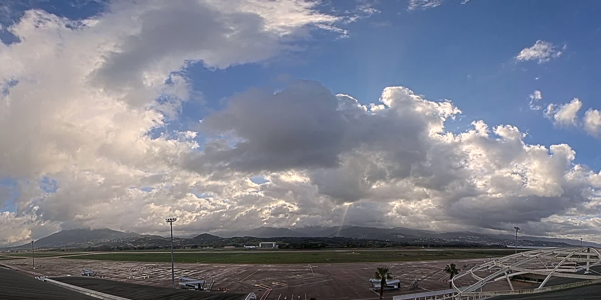 A partly cloudy sky over an airport tarmac with mountains in the distance.