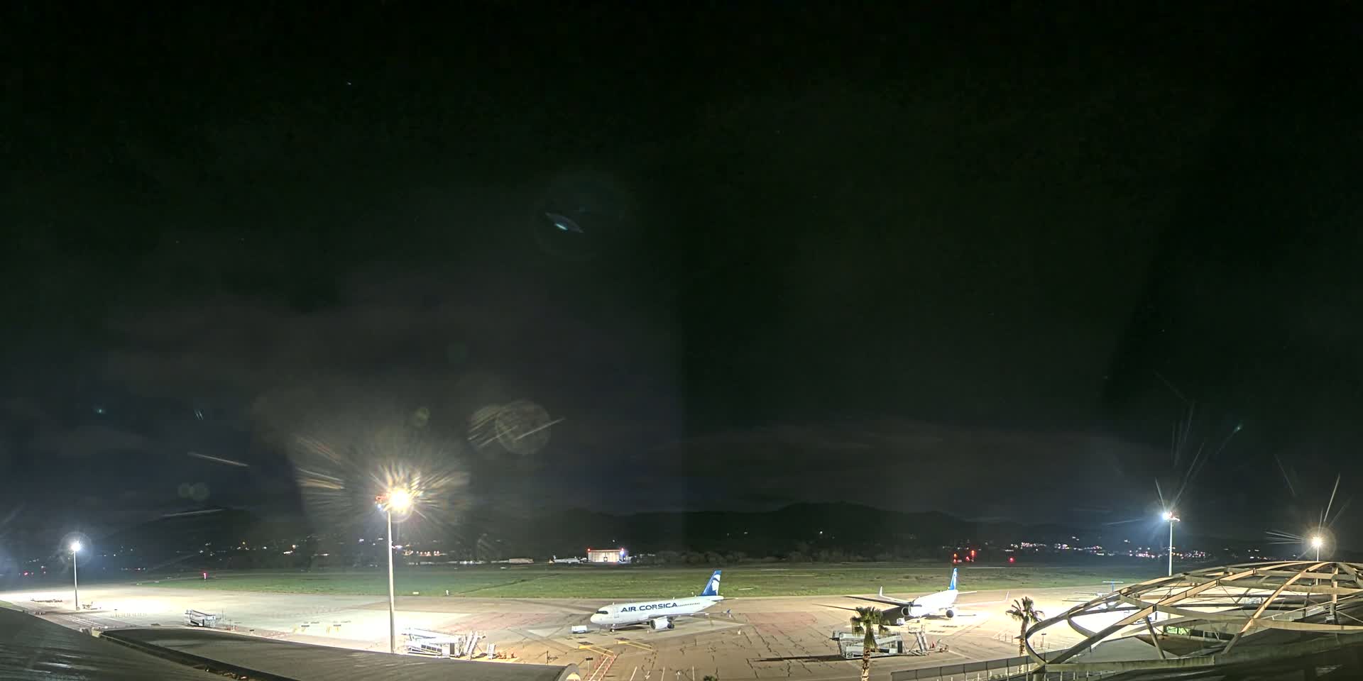 At night, two airplanes sit on a tarmac at an airport under a mostly clear, dark sky.