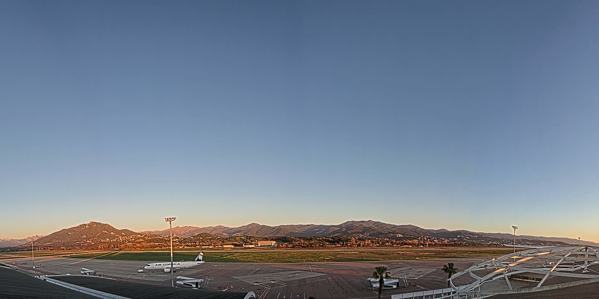 A clear, dusk sky over an airport tarmac with a single airplane parked, backed by a range of mountains.