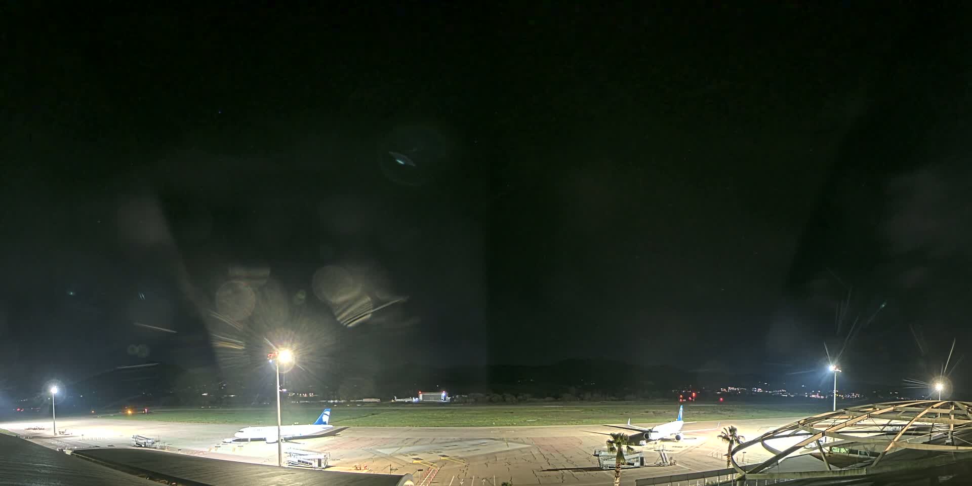 Two airplanes are parked on a brightly lit tarmac at night under a dark, clear sky.