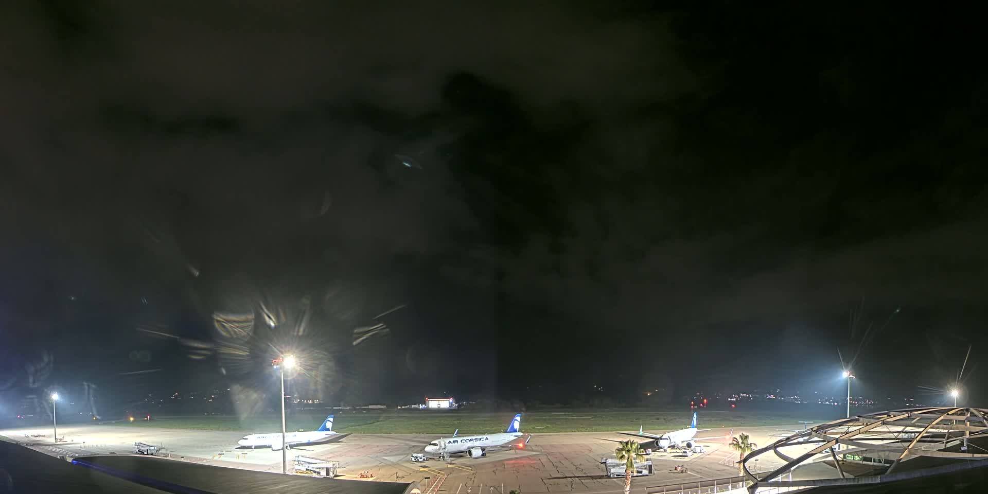 Two airplanes are parked on a tarmac at night under a dark, cloudy sky.