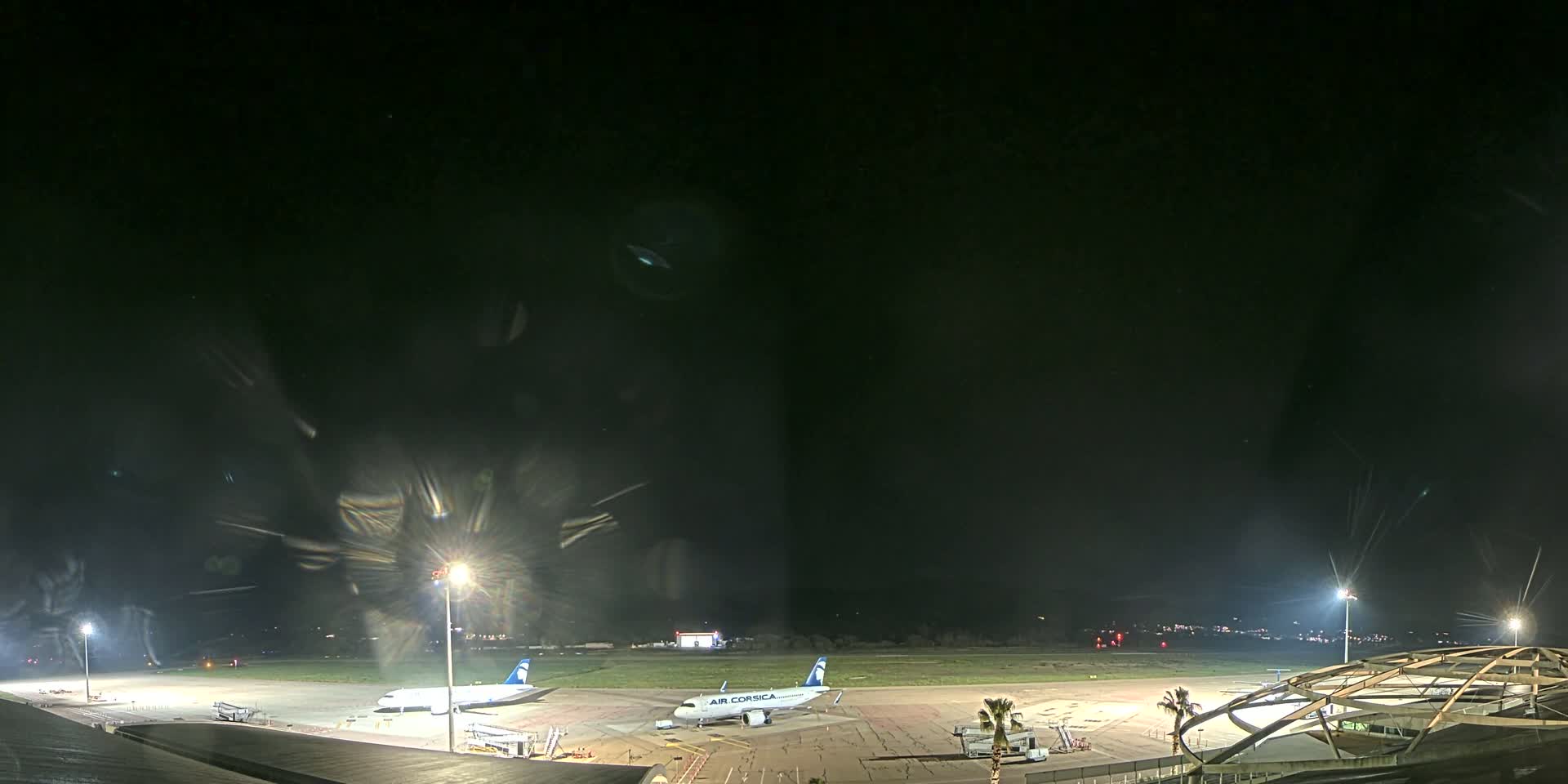 At night, two airplanes are parked on a brightly lit airport tarmac under a clear, dark sky.