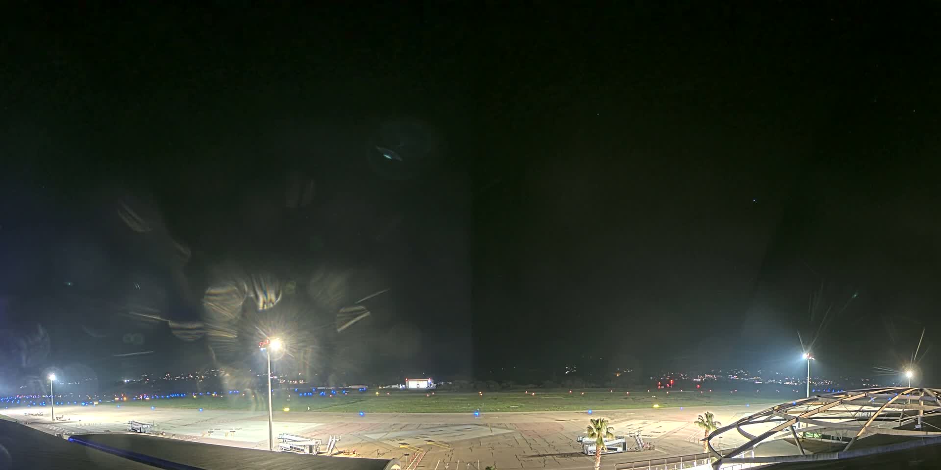 A nighttime view of an airport tarmac, illuminated by bright lights, with a clear, dark sky above.
