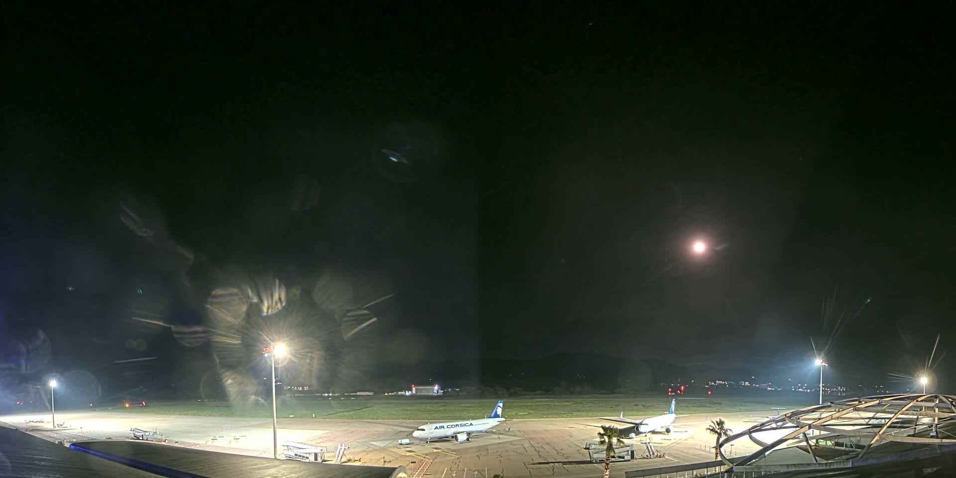 A nighttime view of an airport tarmac with a single airplane parked near a terminal building under a clear, moonlit sky.