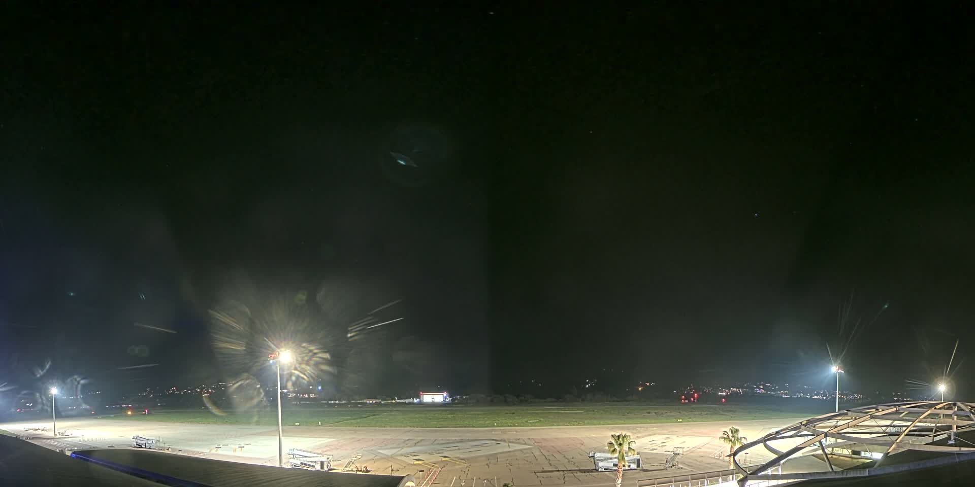 A nighttime view of an airport tarmac with several lights illuminating the ground and a portion of a building visible in the lower right corner.