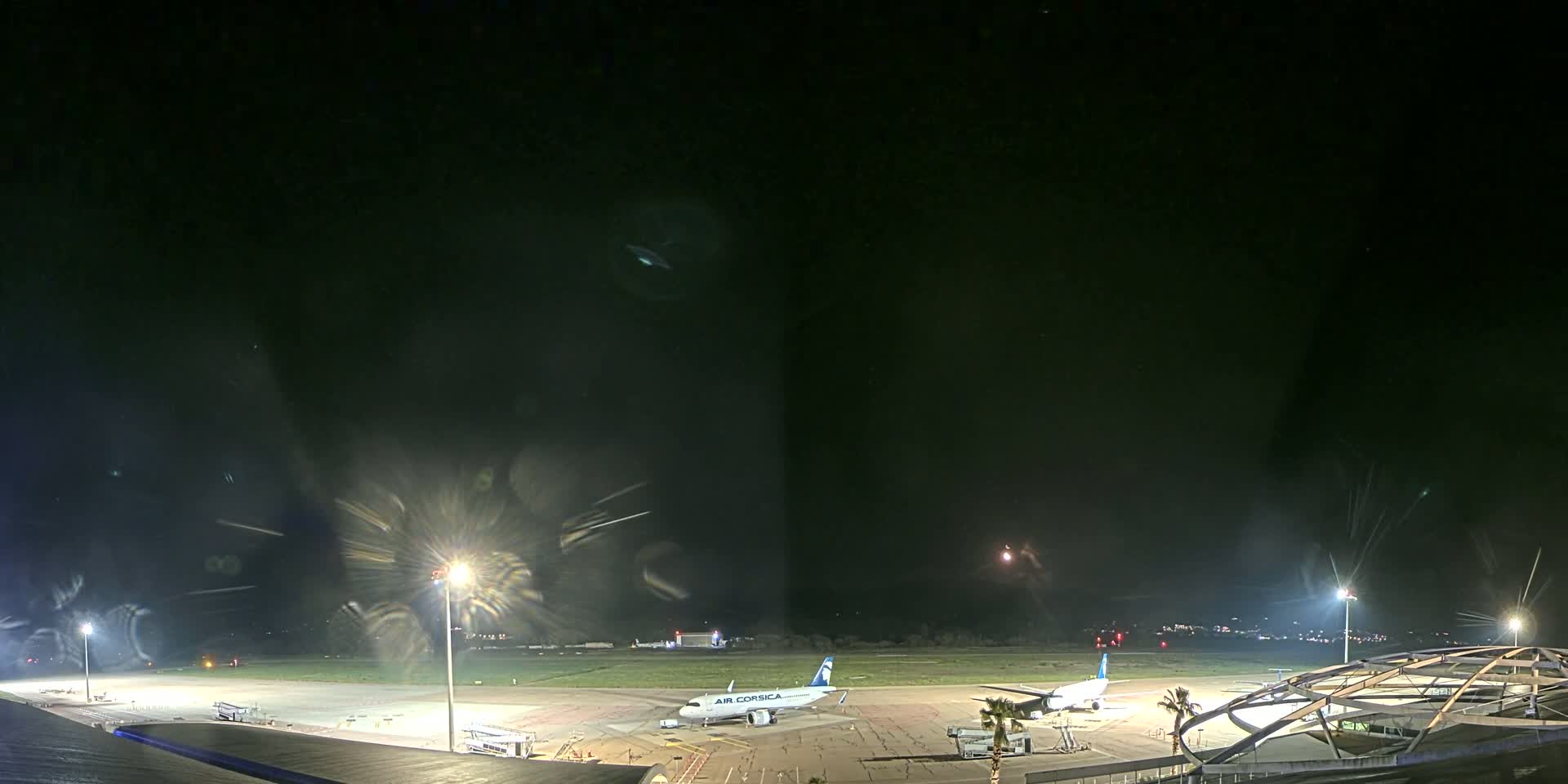 A nighttime view of an airport tarmac with two airplanes parked, illuminated by bright lights under a dark, clear sky.