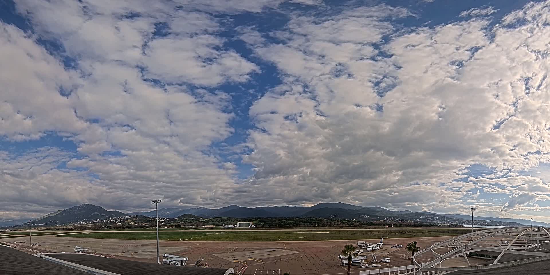 A mostly cloudy sky over an airport tarmac with mountains in the distance.