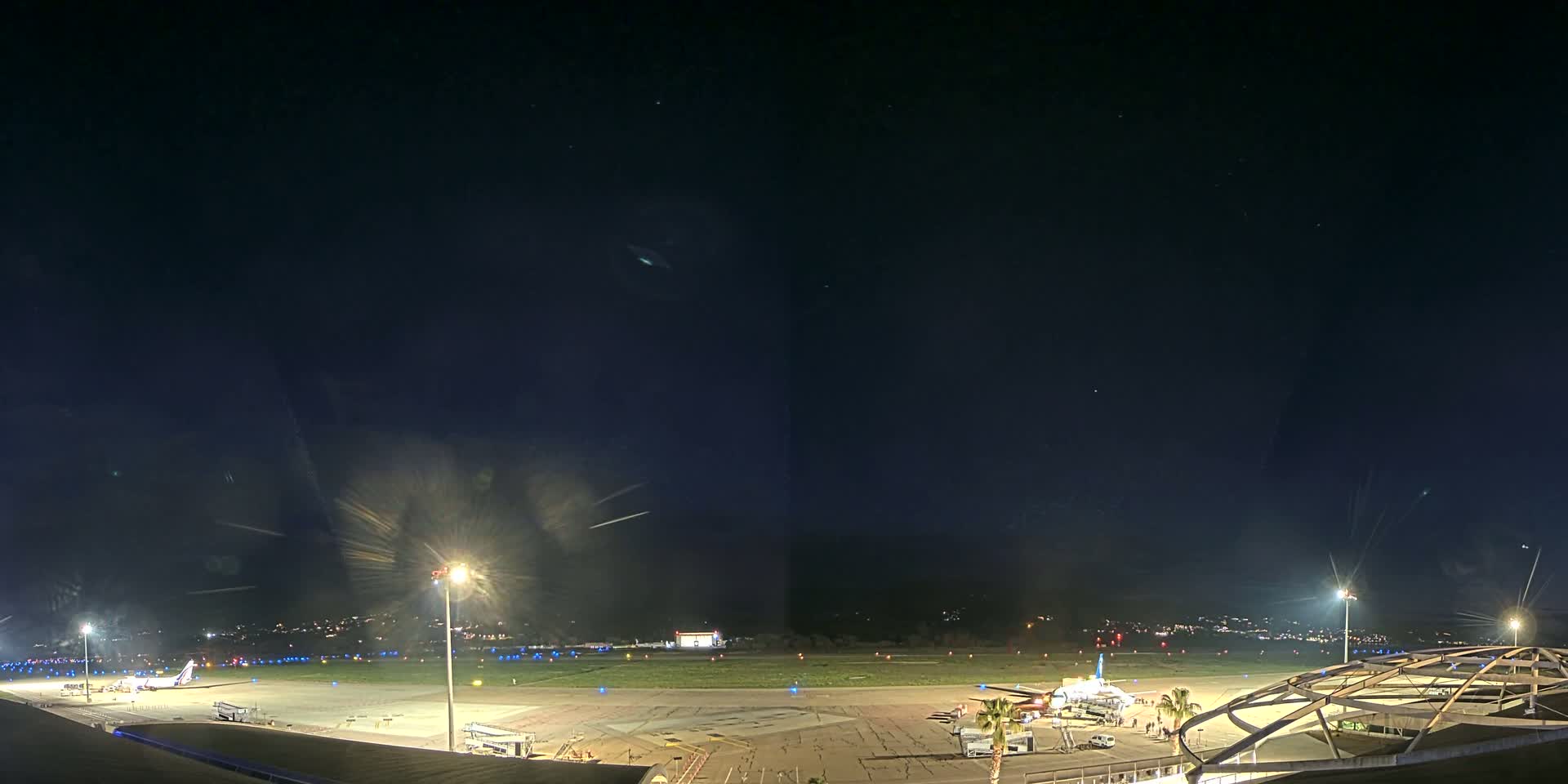 A nighttime view of an airport tarmac with a single airplane parked near a terminal building under a clear, starry sky.