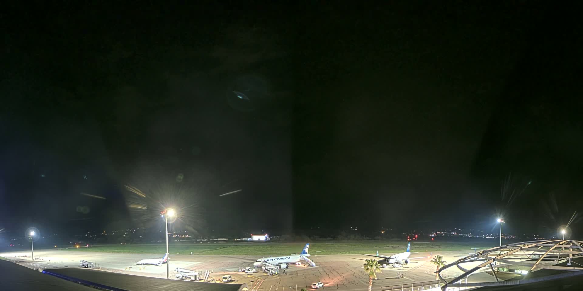 A nighttime view of an airport tarmac with two airplanes parked near passenger boarding bridges, under a dark, clear sky.