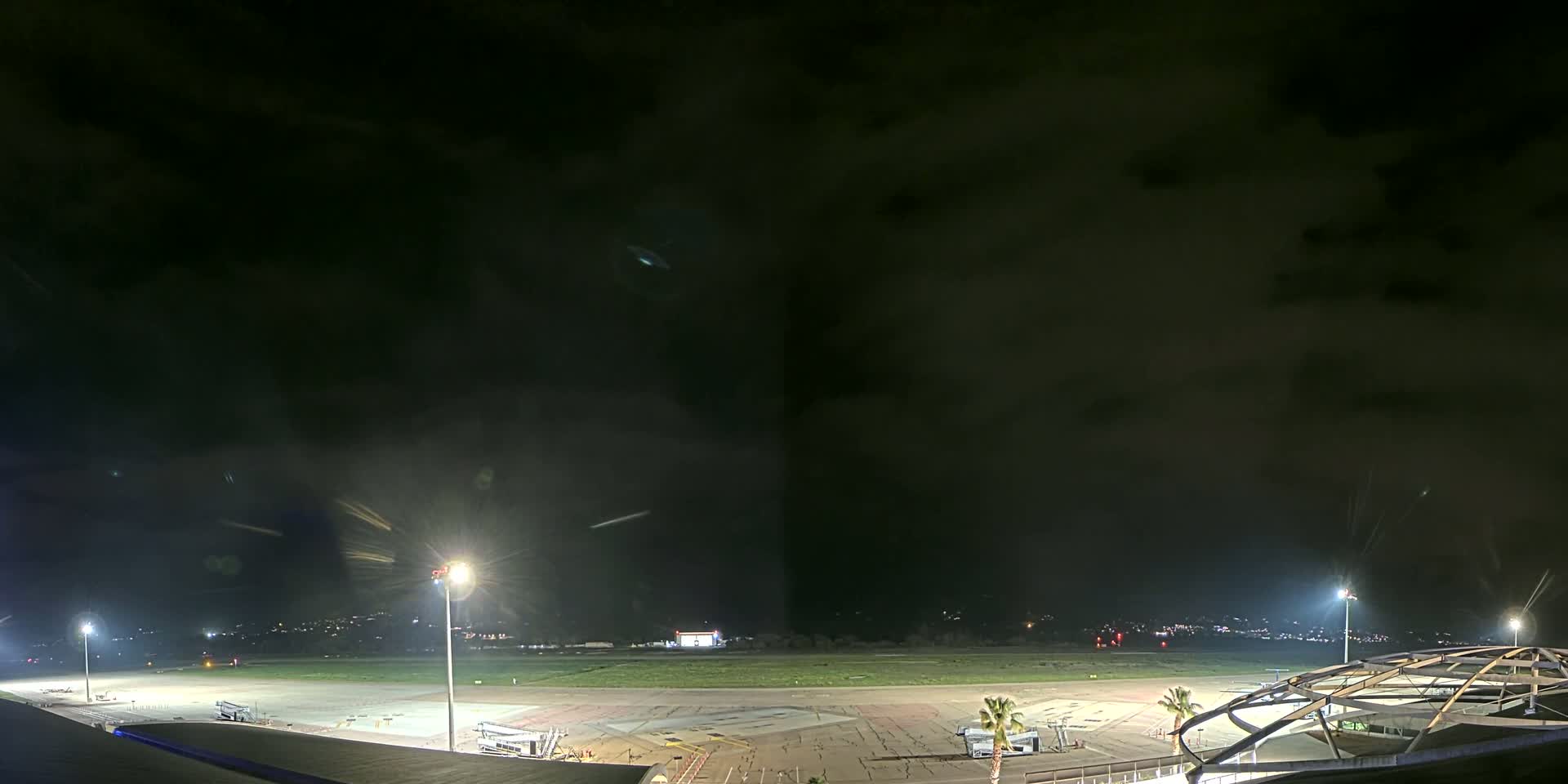 A nighttime view of an airport tarmac with several lights illuminating the area under a dark, cloudy sky.