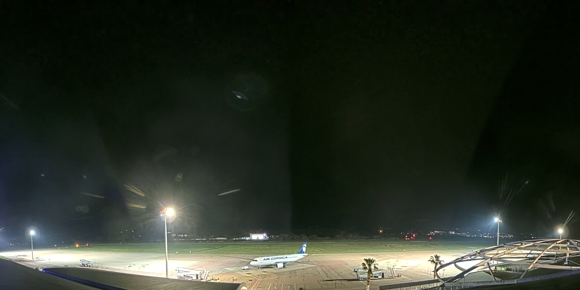 A nighttime view of an airport tarmac with a single airplane parked near a terminal building under clear, dark skies.